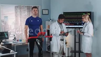 两名混合赛医生讨论运动员在运动实验室做跑步机测试的心电图数据